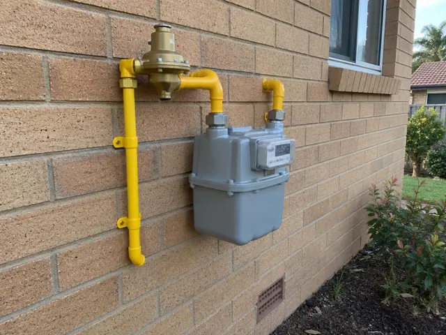 Exterior gas meter and yellow pipework on a brick house wall in Dee Why